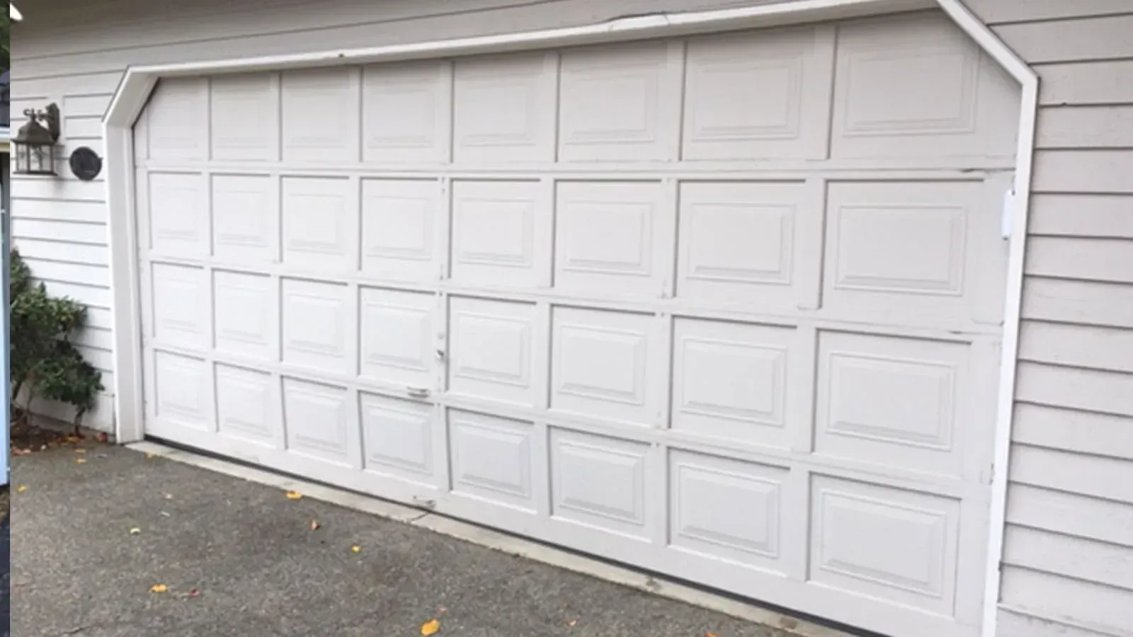 A white garage door with a grid of rectangular panels set into the side of a house with light gray horizontal siding.