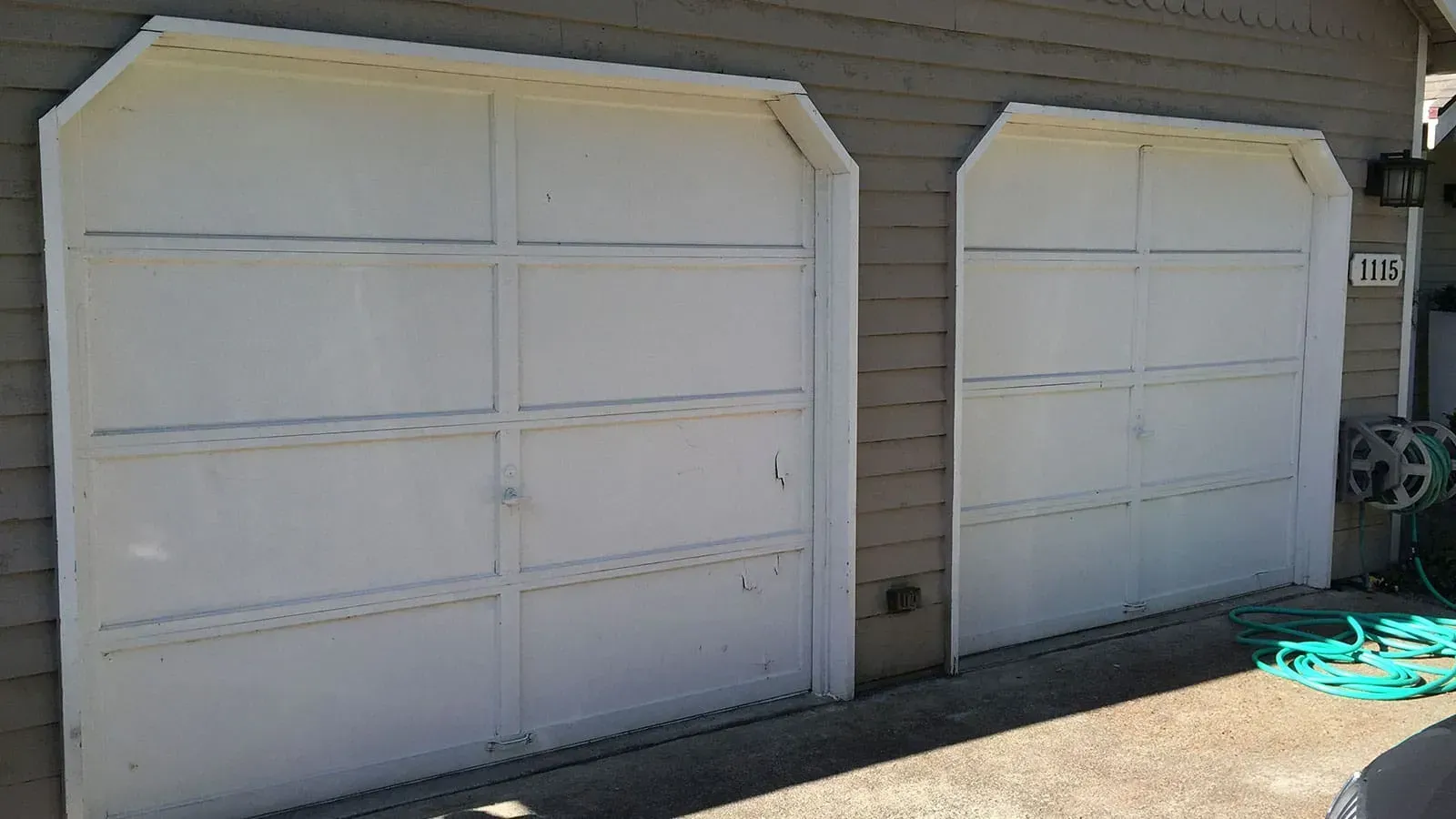 Two white, multi-panel residential garage doors with angled top corners set into a grey-sided exterior wall.