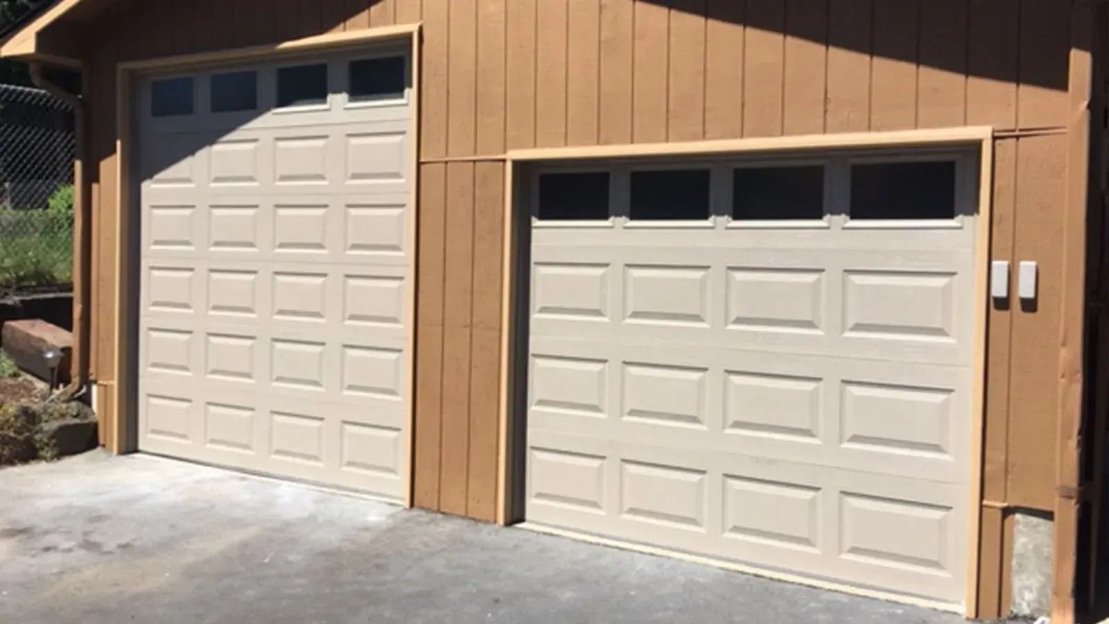 Two tan, paneled garage doors with upper windows on a tan building.