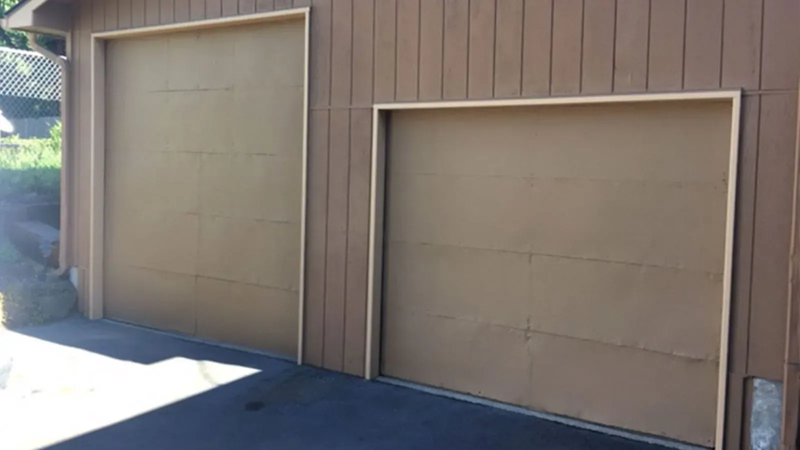 Two brown garage doors of unequal height set into a brown wooden building exterior.