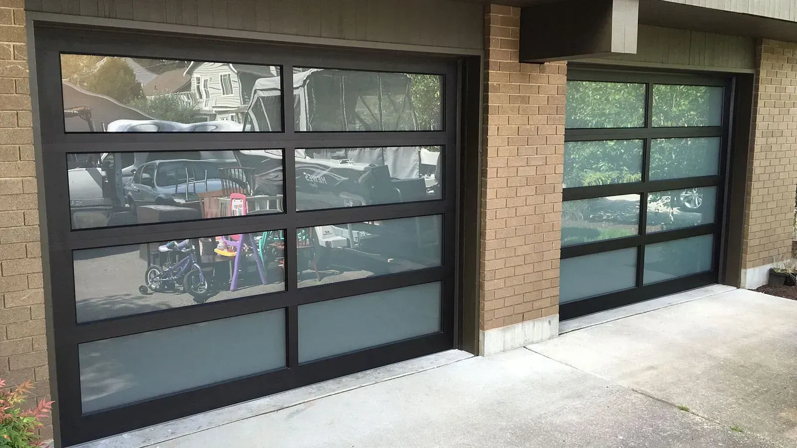 Two modern black-framed garage doors with horizontal, frosted glass panels installed on a brick building exterior.