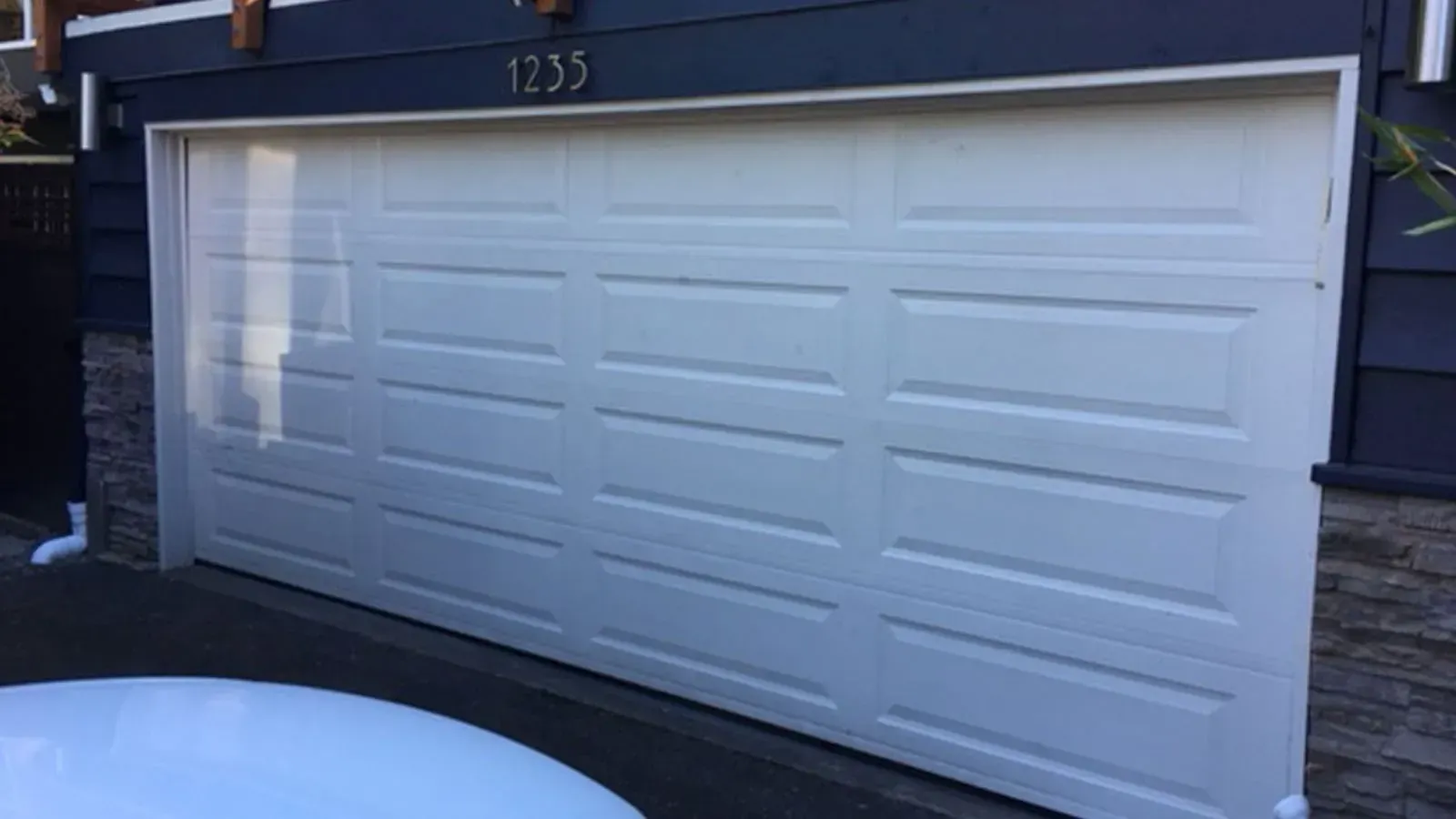 A white, multi-panel garage door on a house with dark siding and stone accents, displaying the house number 1235.