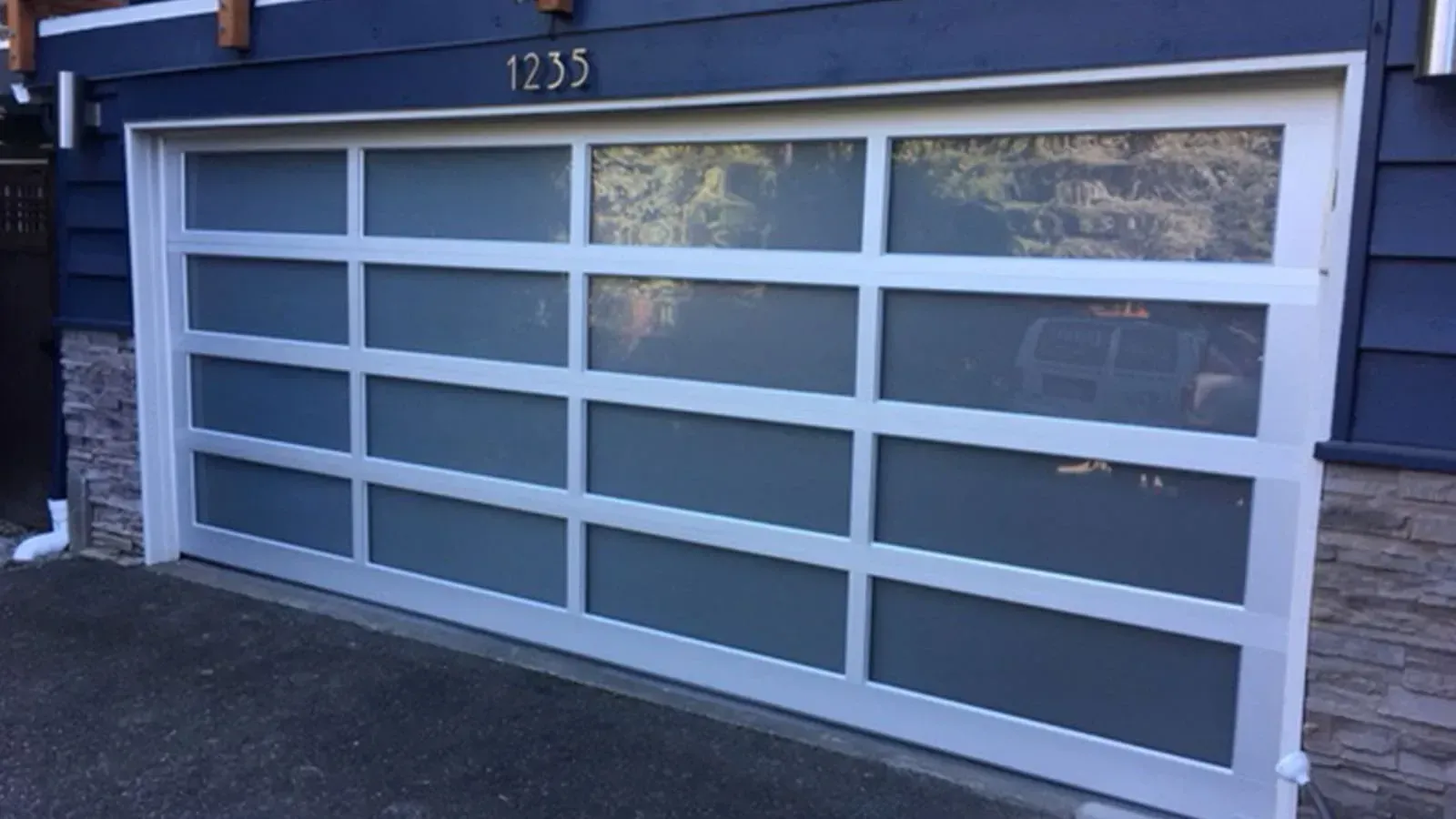 A modern white-framed garage door with four horizontal rows of rectangular frosted glass panels set in a dark blue house.