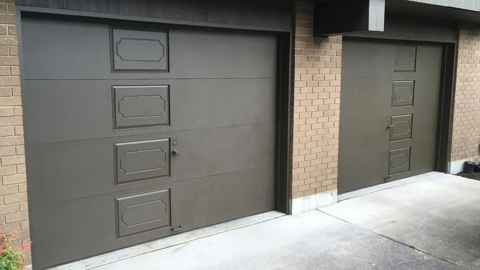 Two brown, multi-panel residential garage doors with rectangular decorative accents, set against a tan brick exterior.
