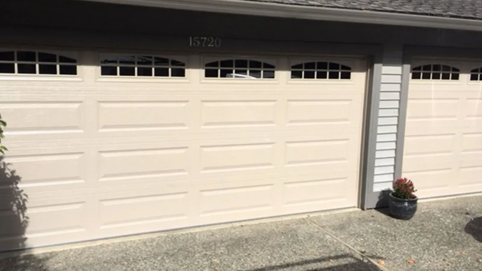 A tan two-car garage door with windows along the top panels, situated next to a smaller single garage door.