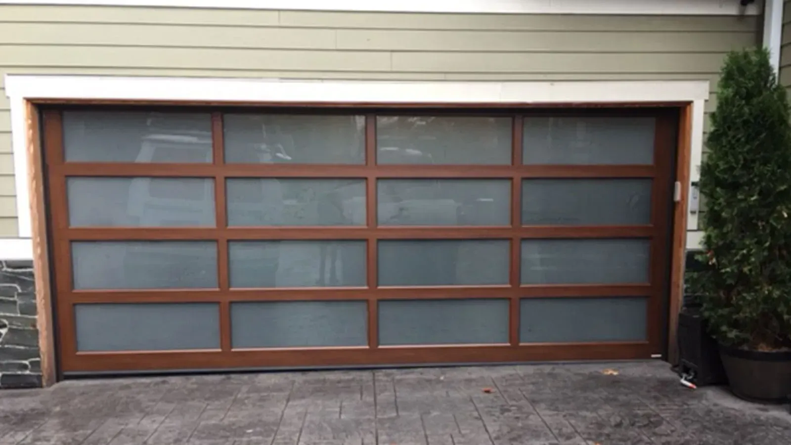 A modern, four-section garage door with a brown frame and frosted glass panels set in a home exterior.