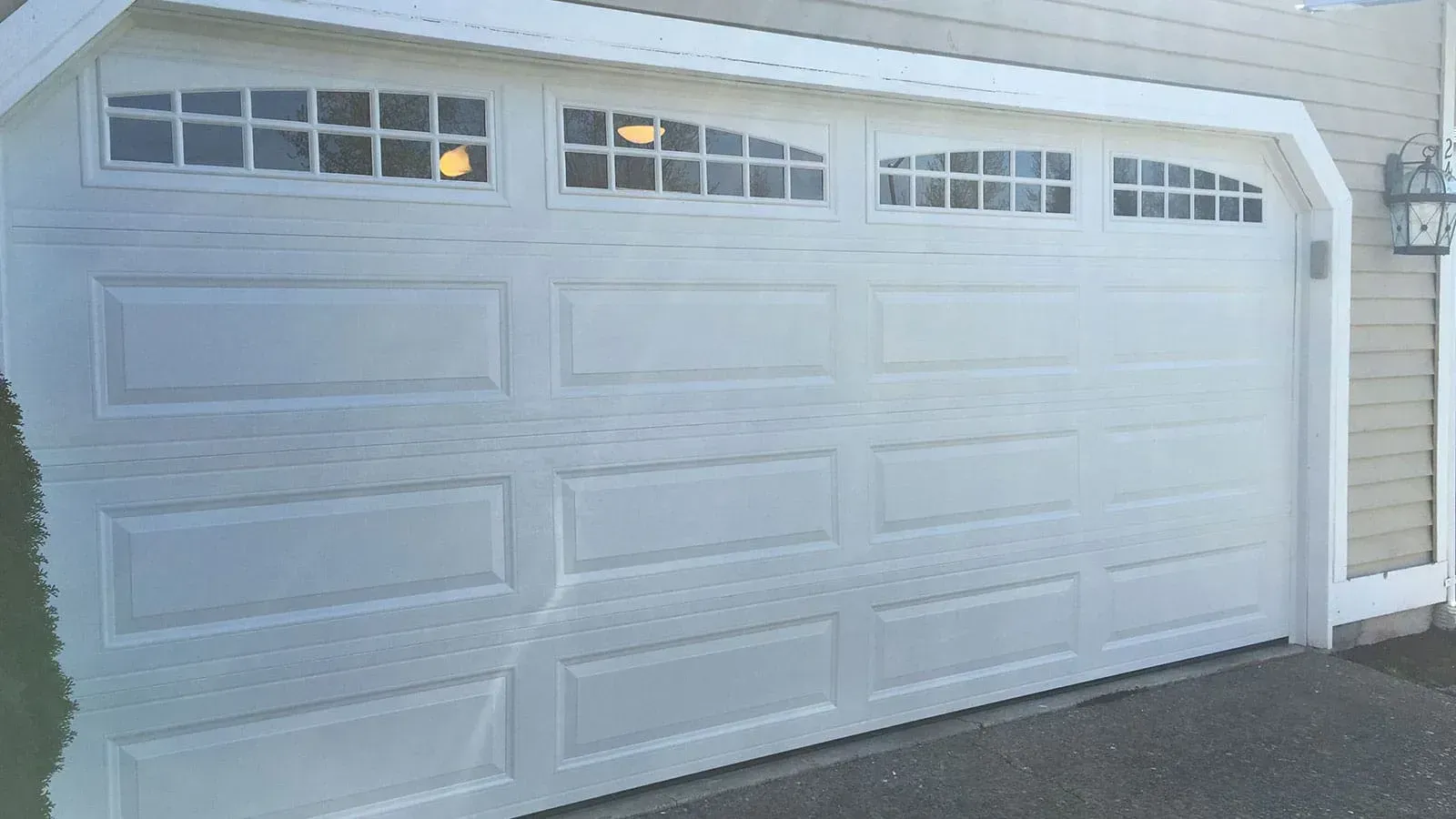 A white residential garage door with four rectangular panels across and a row of windows with grid inserts at the top.