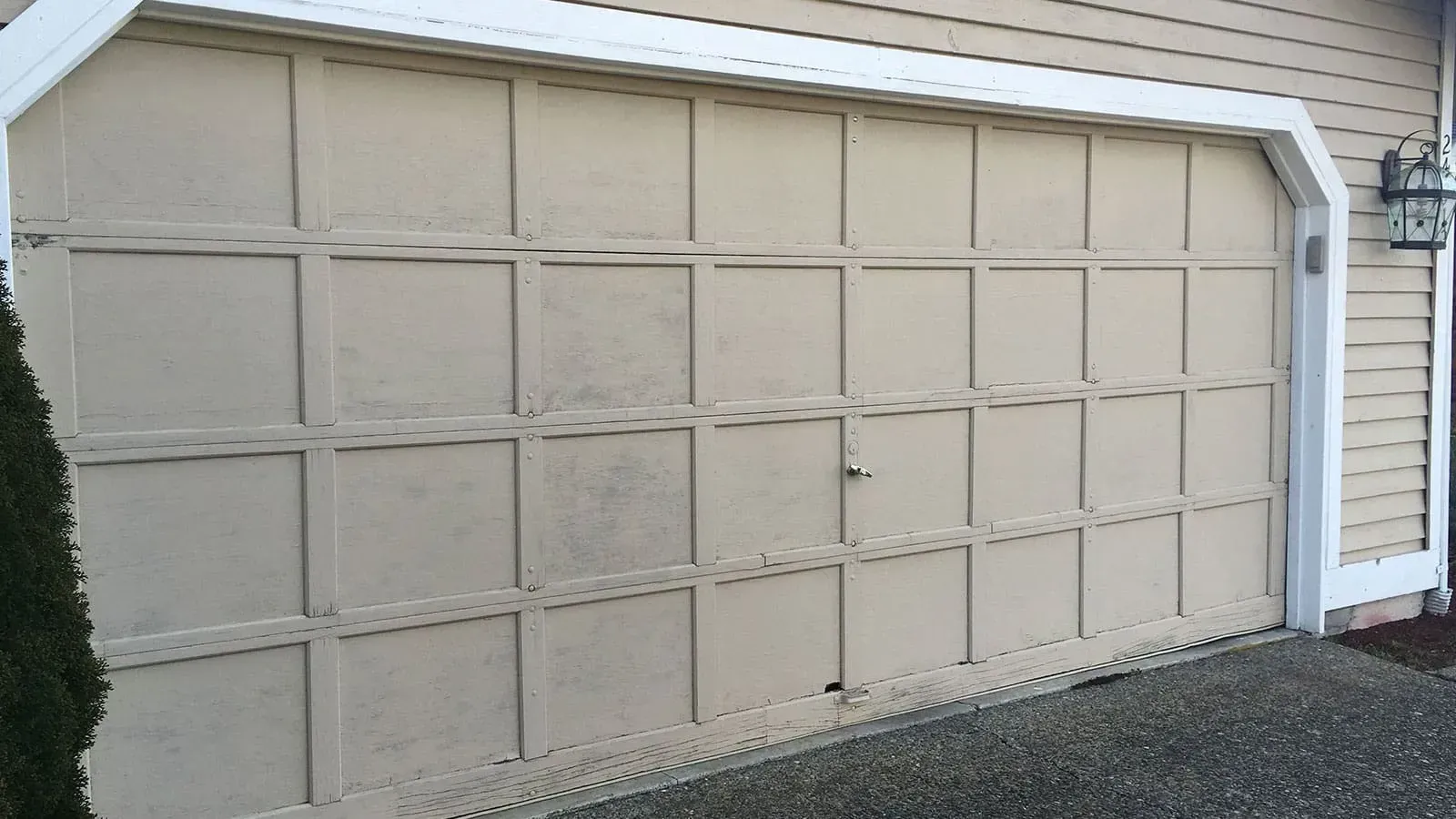 A beige, paneled garage door with white trim, situated on the side of a house next to a gravel driveway.