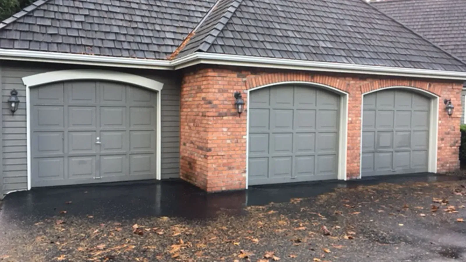 A house exterior featuring three grey garage doors set against a brick and siding facade with a shingled roof.