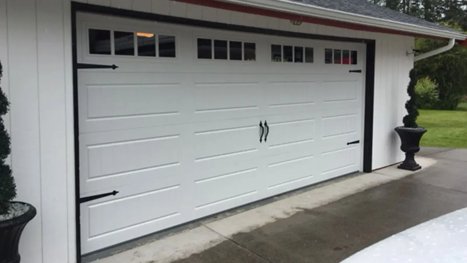 White carriage-style garage door with black decorative hinges, handles, and windows on a residential exterior.