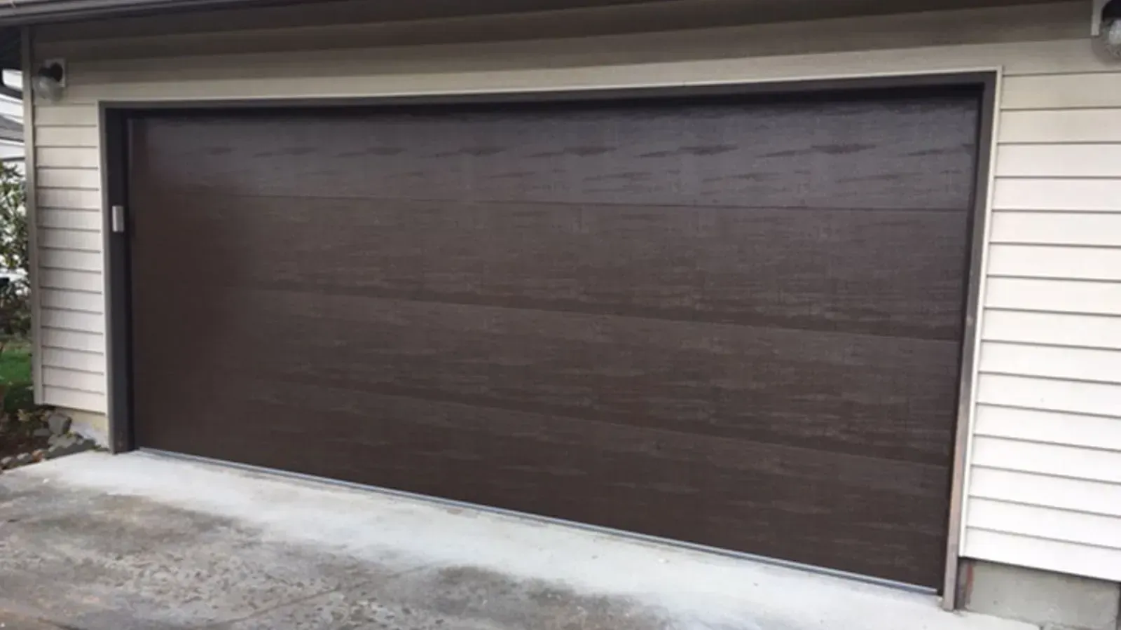 A dark brown, horizontal-panel garage door set in a beige-sided residential exterior.
