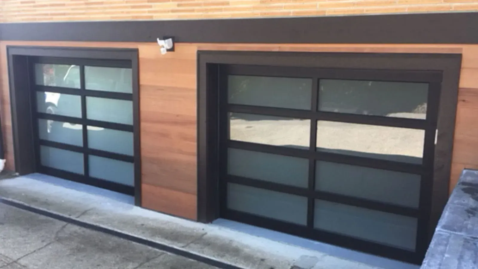 Two modern garage doors with black metal frames and frosted glass panels, set in a light wood-paneled wall.