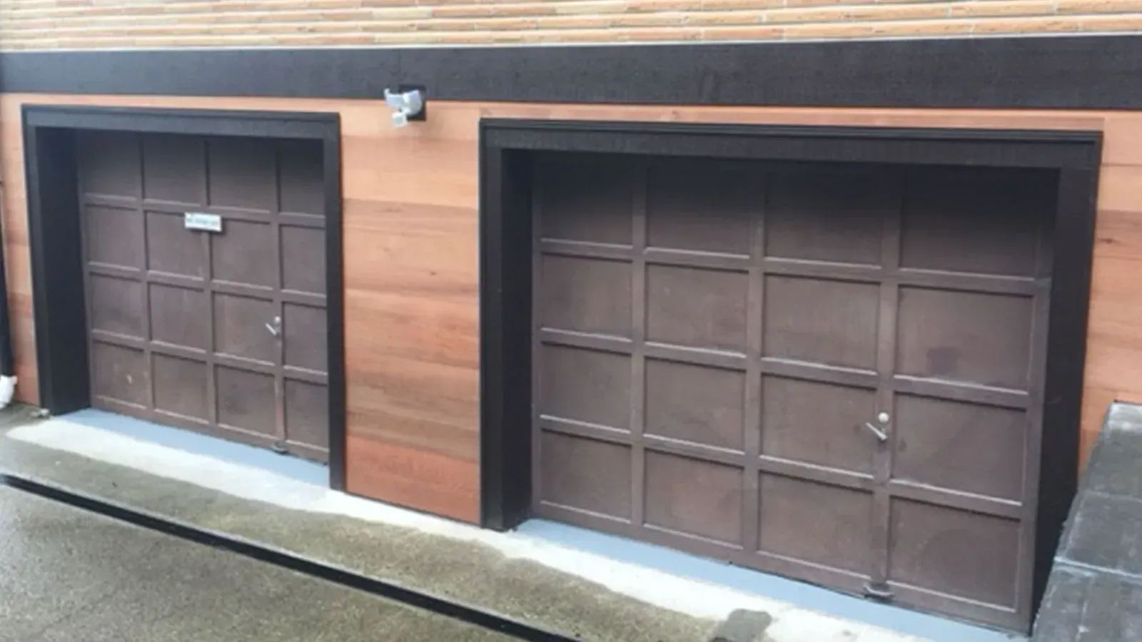 Two brown, panelled garage doors set into a horizontal wooden-planked wall with dark trim.