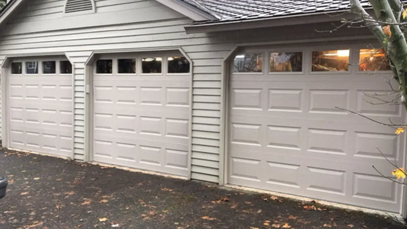 A light-colored three-car garage with white paneled doors and windows on a paved driveway.