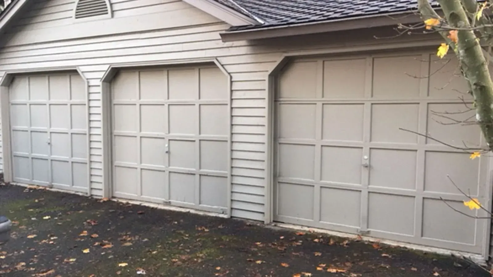 A beige three-car garage with paneled doors and a gabled roof, viewed from an outdoor driveway.