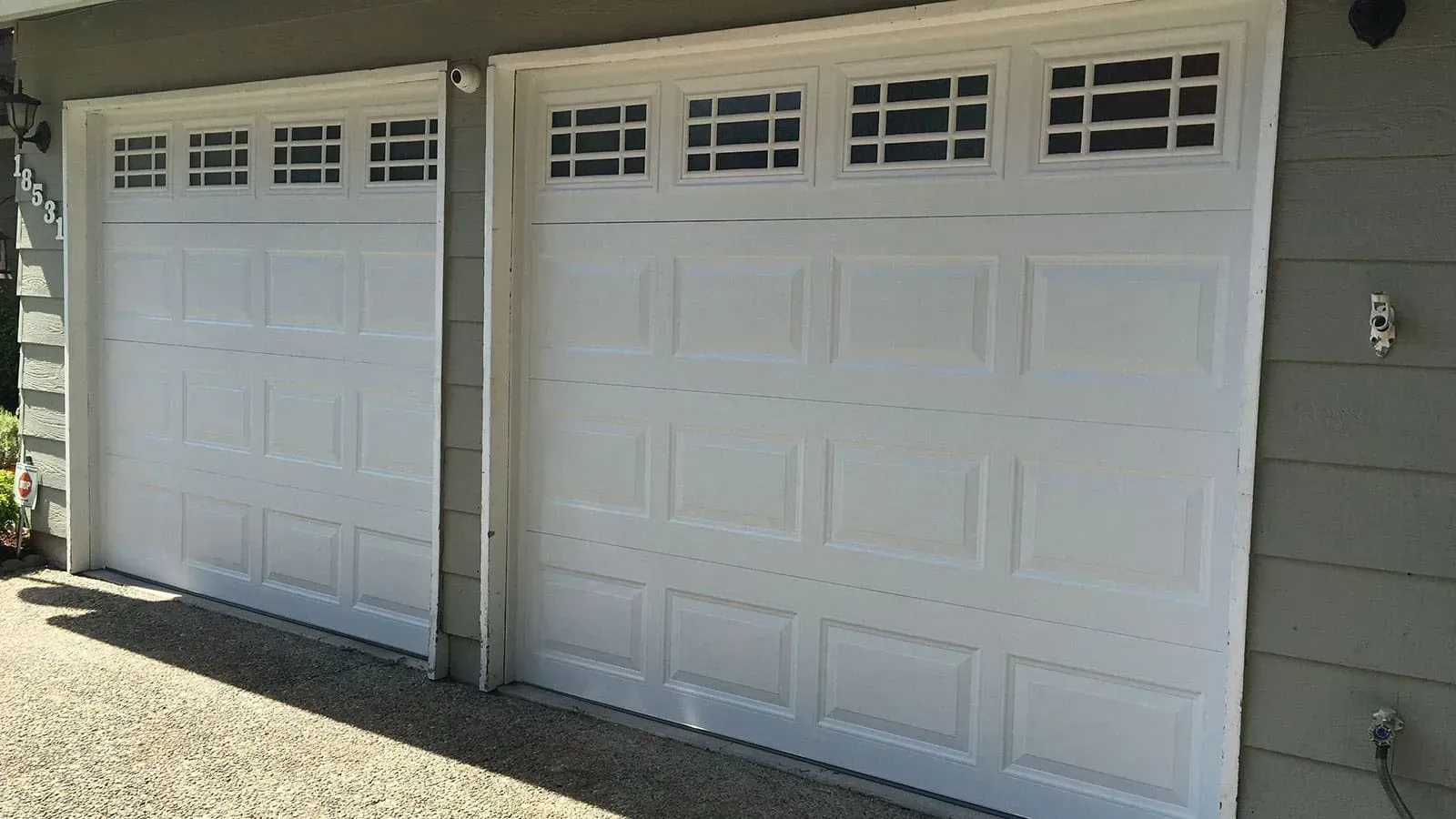 Two white residential garage doors with windows at the top, set against a grey-sided house exterior.