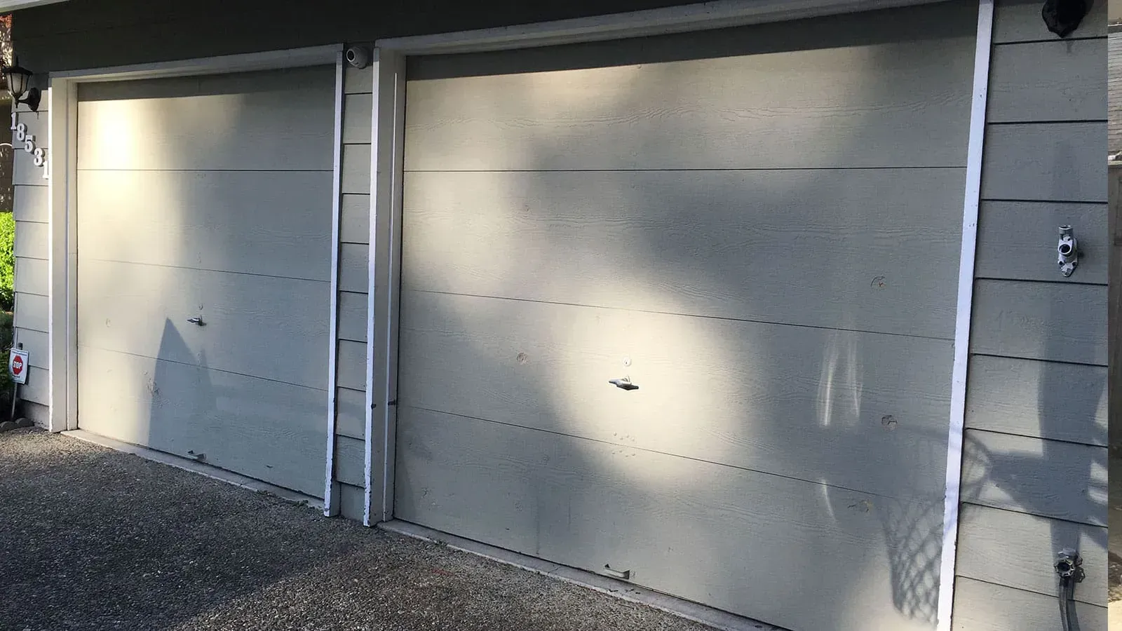 A side-by-side view of two beige, horizontal-paneled garage doors on a light-colored building exterior.