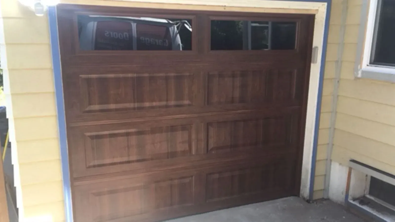 A dark brown, rectangular garage door with four raised panels and two horizontal rows of windows at the top.