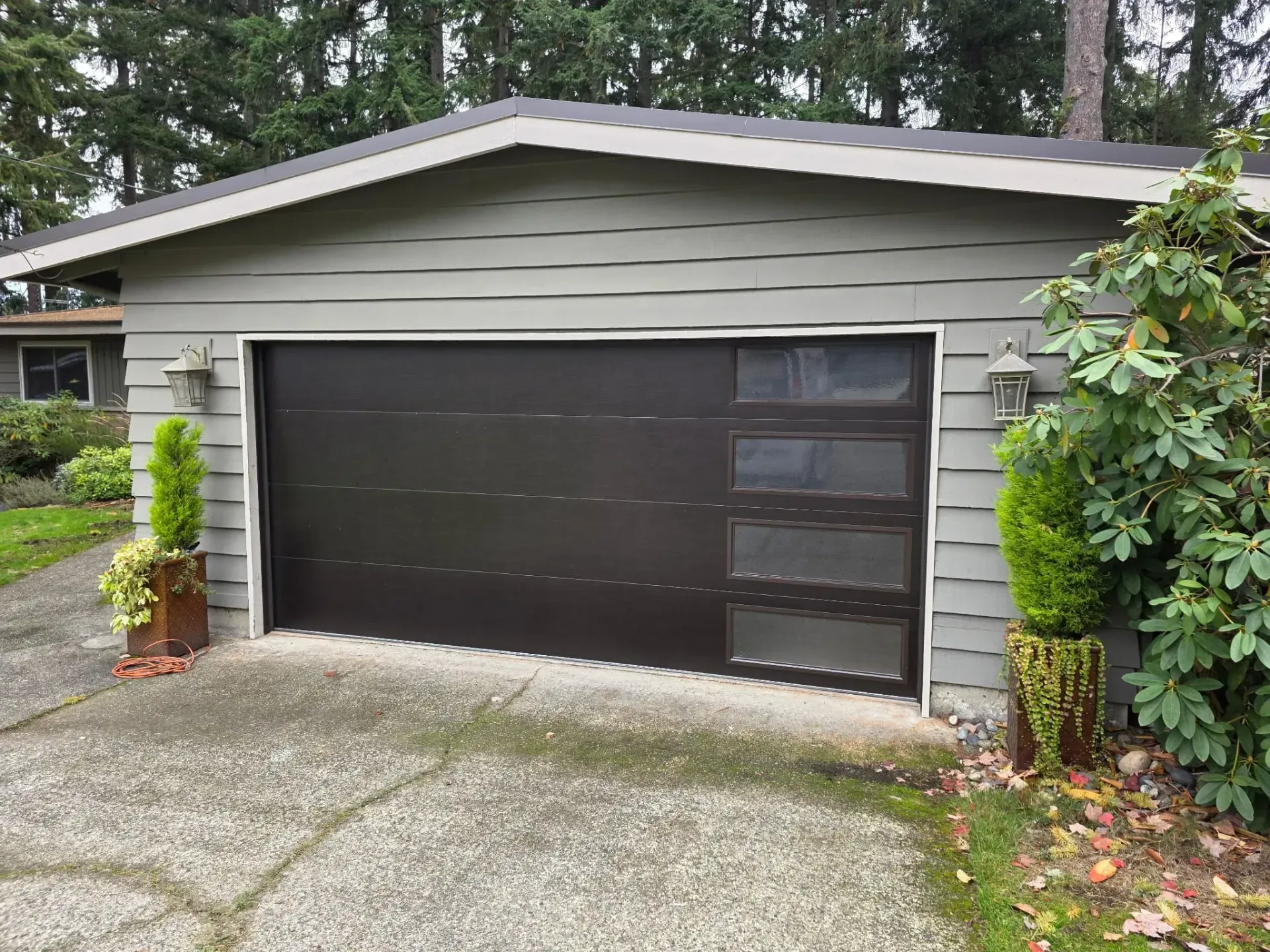 A detached garage with gray horizontal siding and a dark brown garage door featuring a vertical row of four windows.
