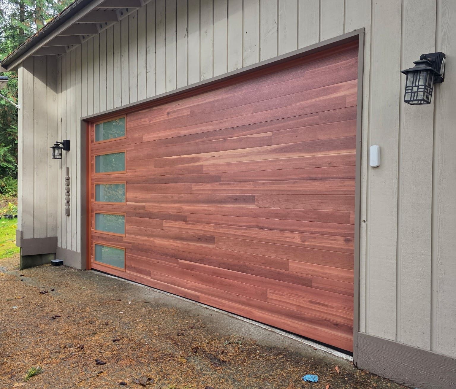 A modern wooden garage door with horizontal planks and a vertical row of five rectangular frosted glass windows.