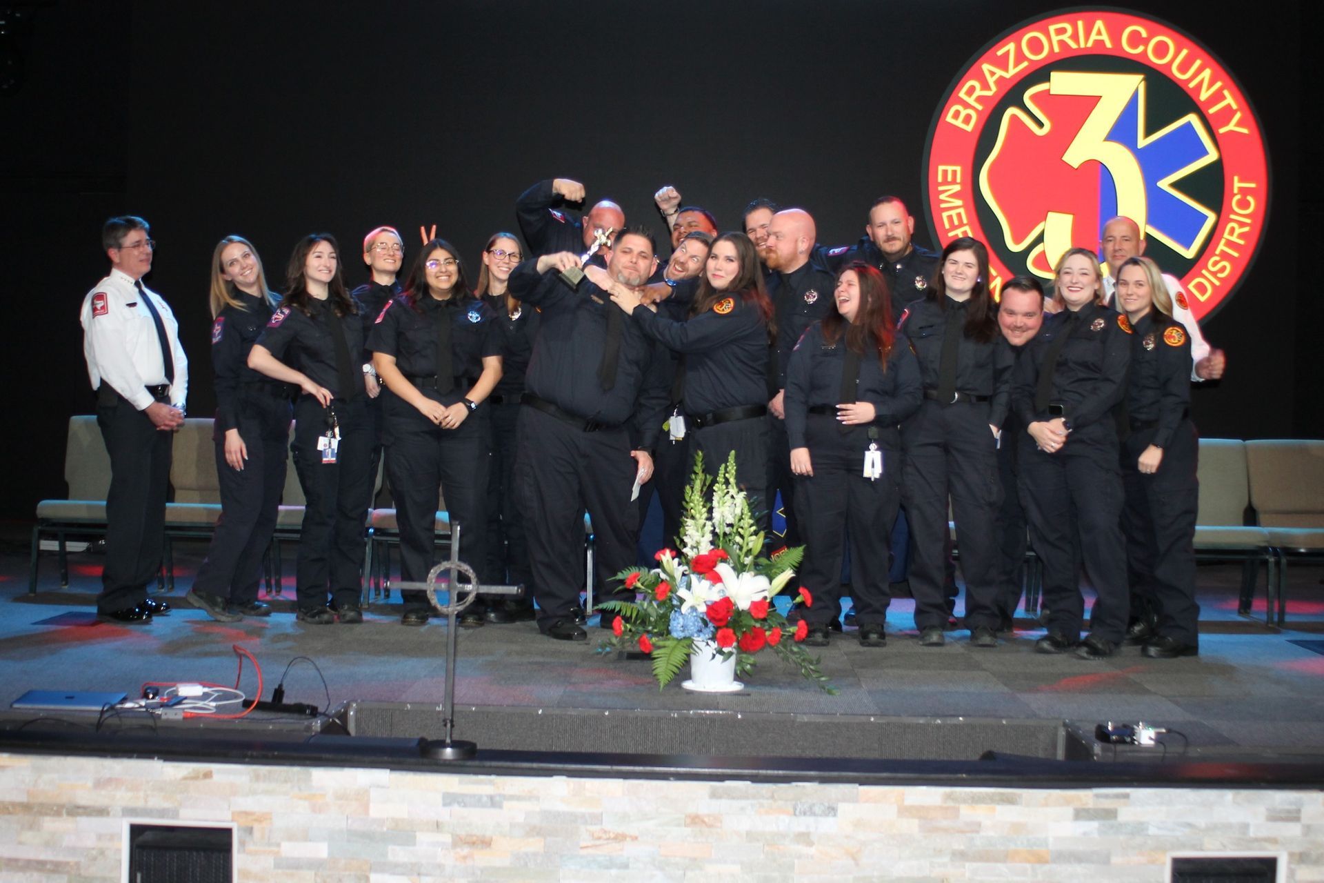 Group of Brazoria County Emergency District personnel, dressed in dark uniforms, on a stage, celebrating.