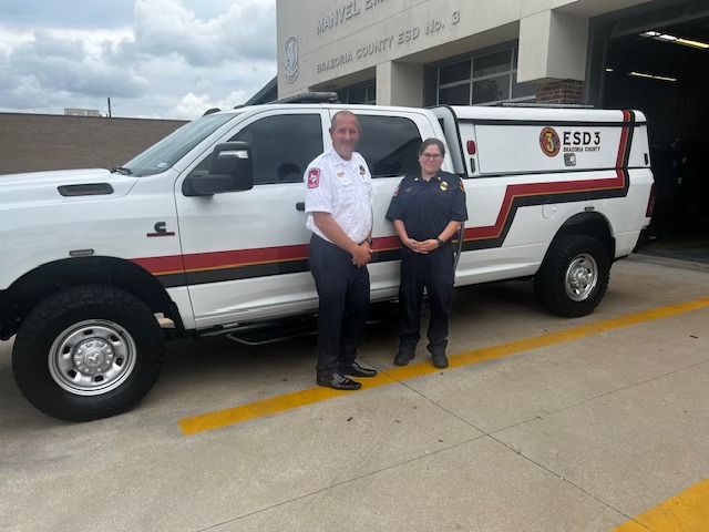 Two EMS personell stand beside a white truck with 