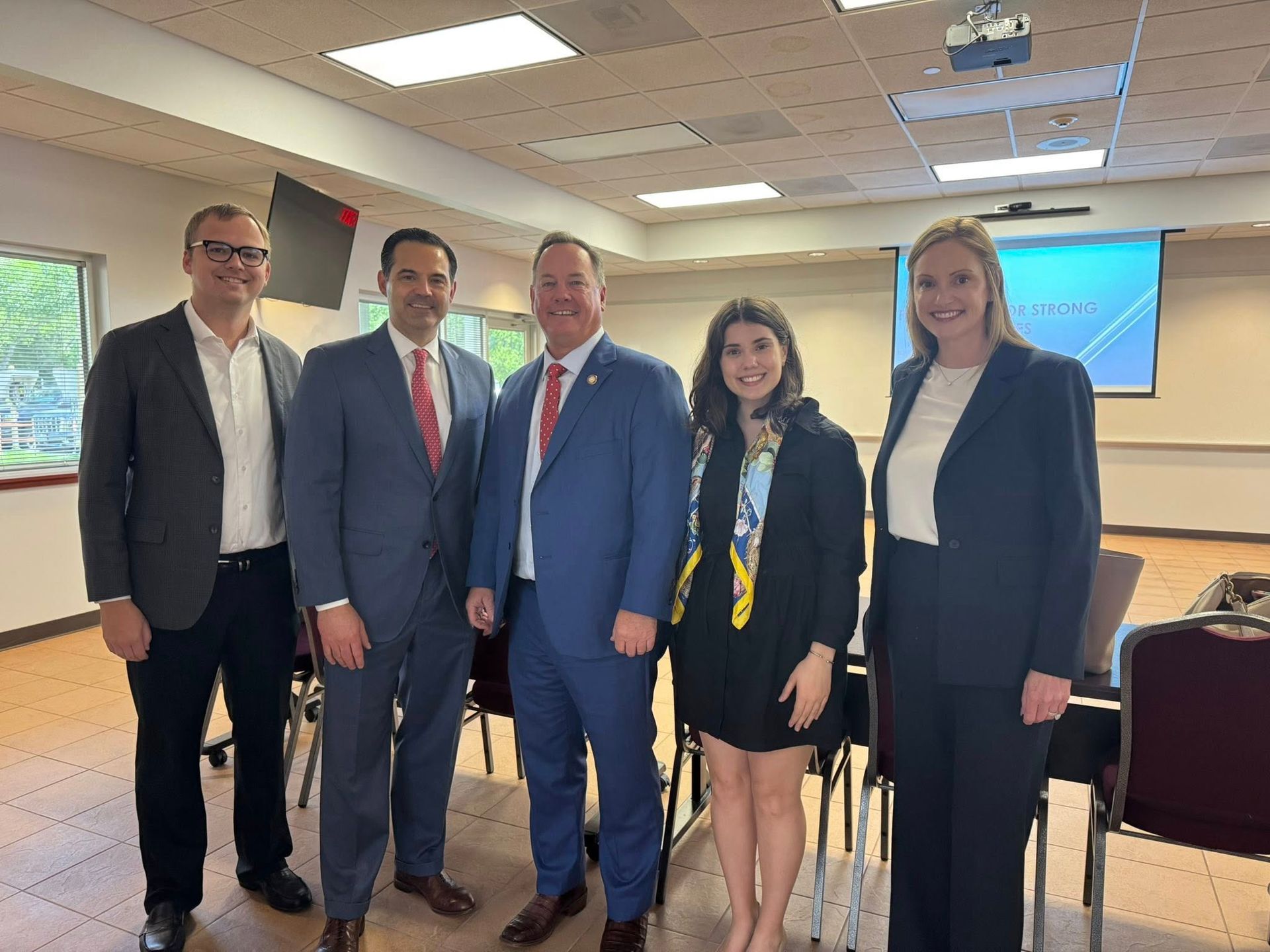 Five individuals in professional business attire stand side-by-side in a well-lit meeting room, posing for a photo.