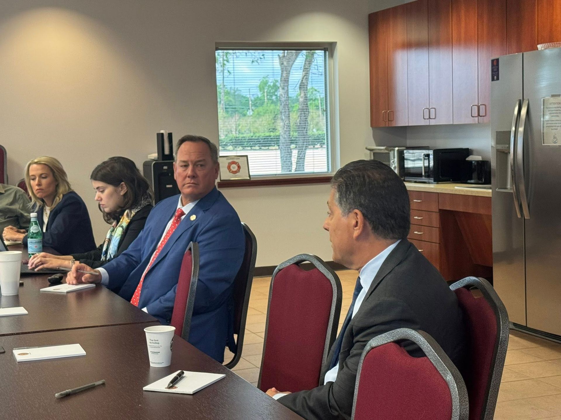 Four people in business attire sit at a conference table in an office, attending a meeting.
