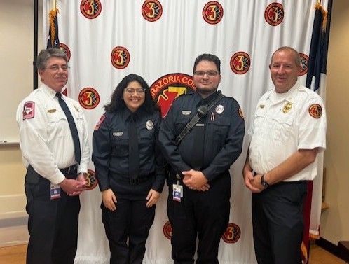 Four people in uniform pose in front of a Brazoria County banner.