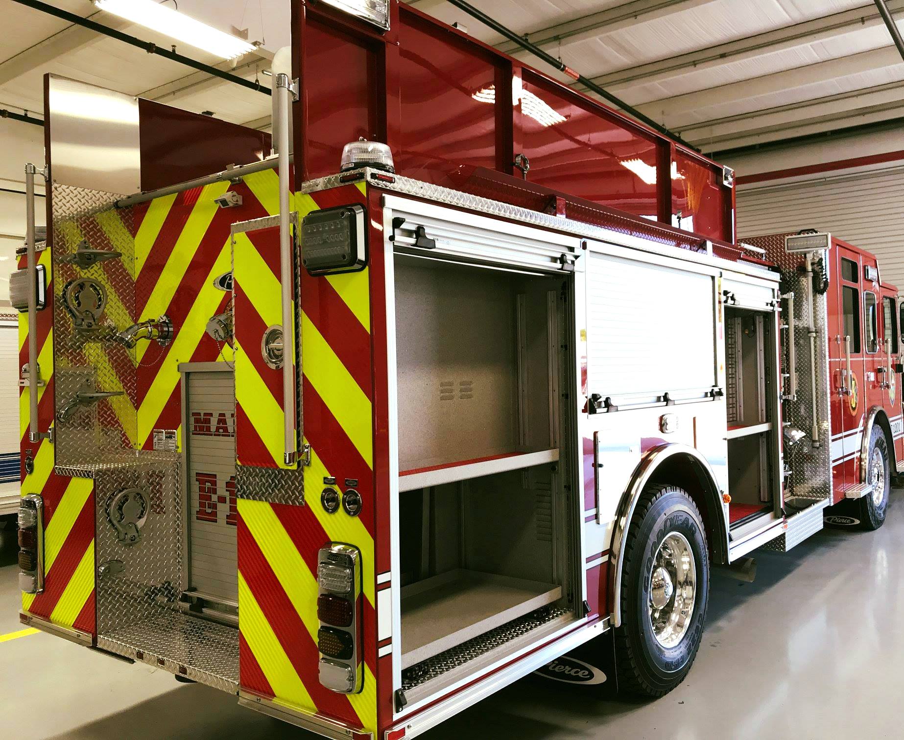 A red and white fire truck with yellow stripes on the back is parked in a garage.