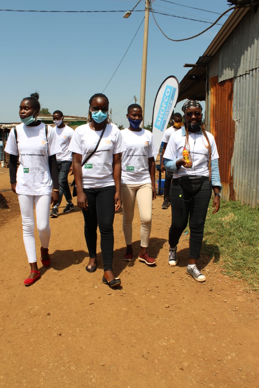A group of people wearing masks are walking down a dirt road.