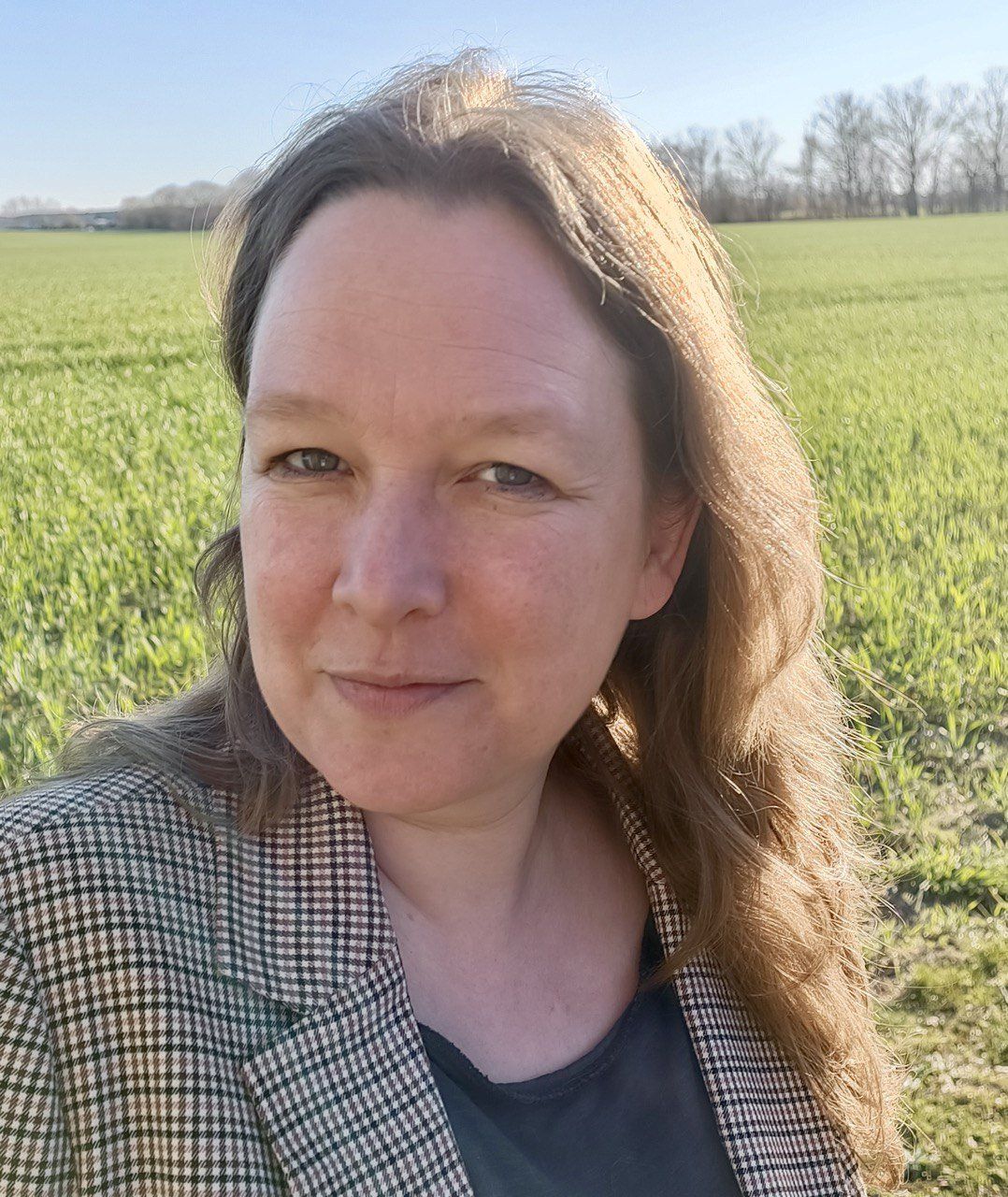 Eine Frau in einer karierten Jacke steht auf einem Feld.
