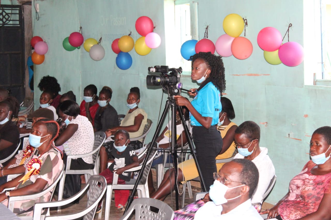 A group of people wearing face masks are sitting in a room with balloons on the wall