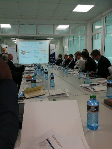 A group of people are sitting around a long table with bottles of water
