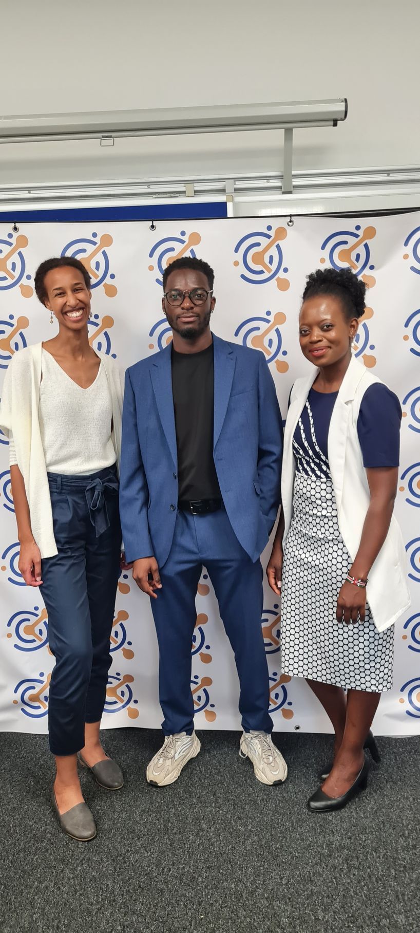 Three people are posing for a picture in front of a wall.