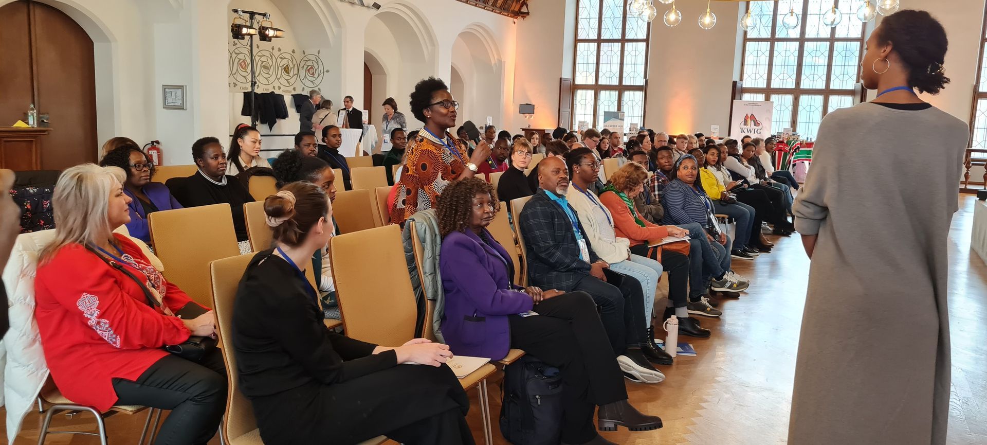 A woman is standing in front of a large group of people sitting in chairs.