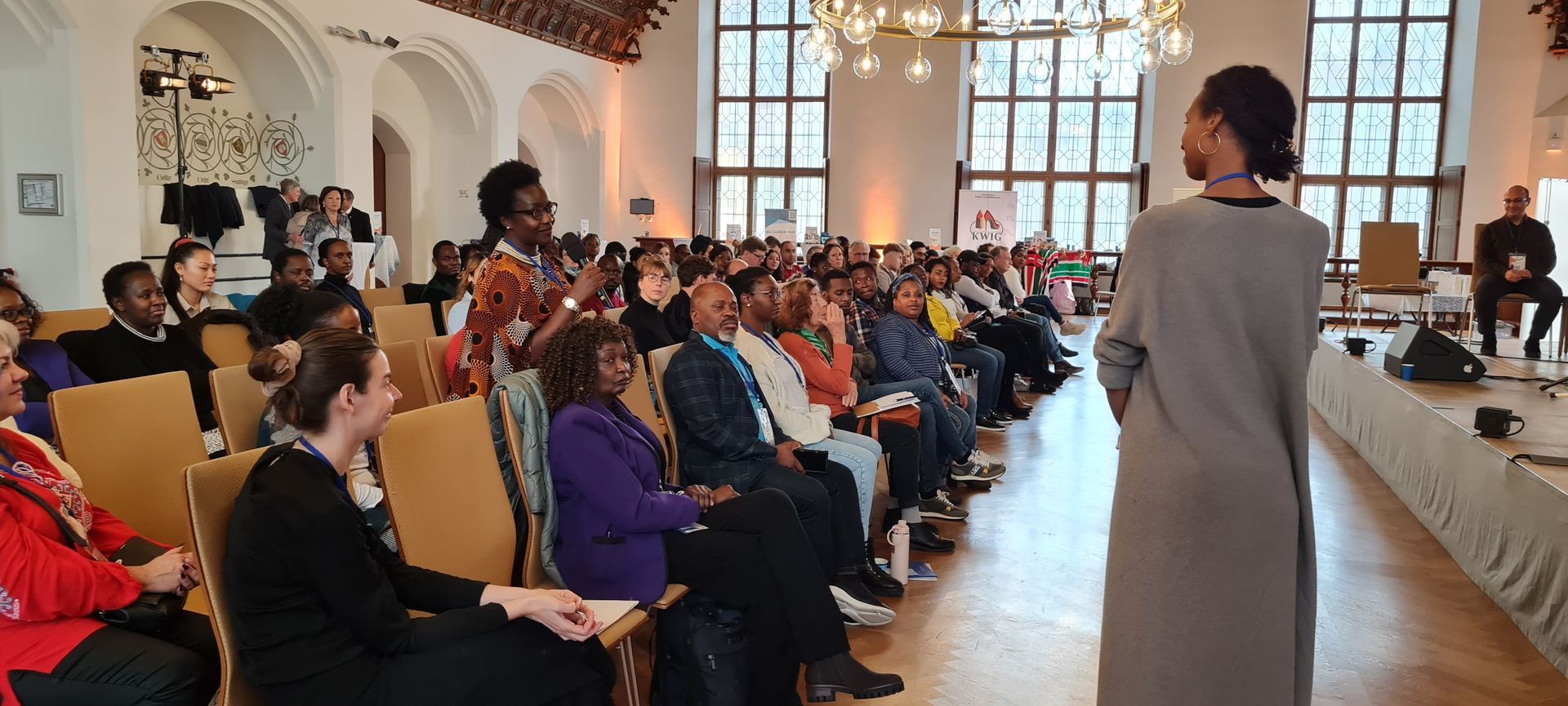 A woman is standing in front of a large group of people sitting in chairs.