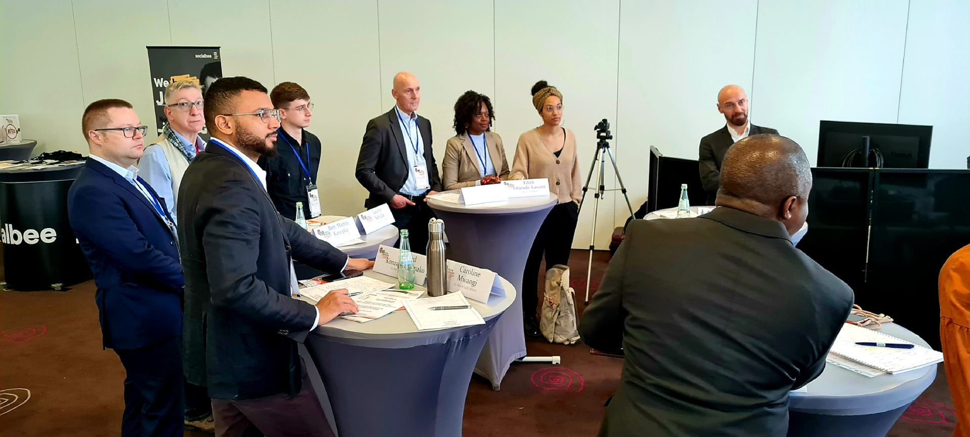 A group of people are standing around tables in a room.
