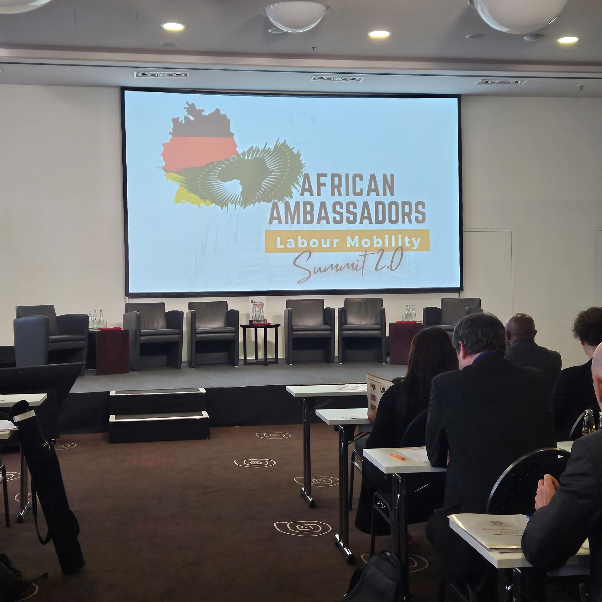 A group of people sitting in front of a large screen that says african ambassadors