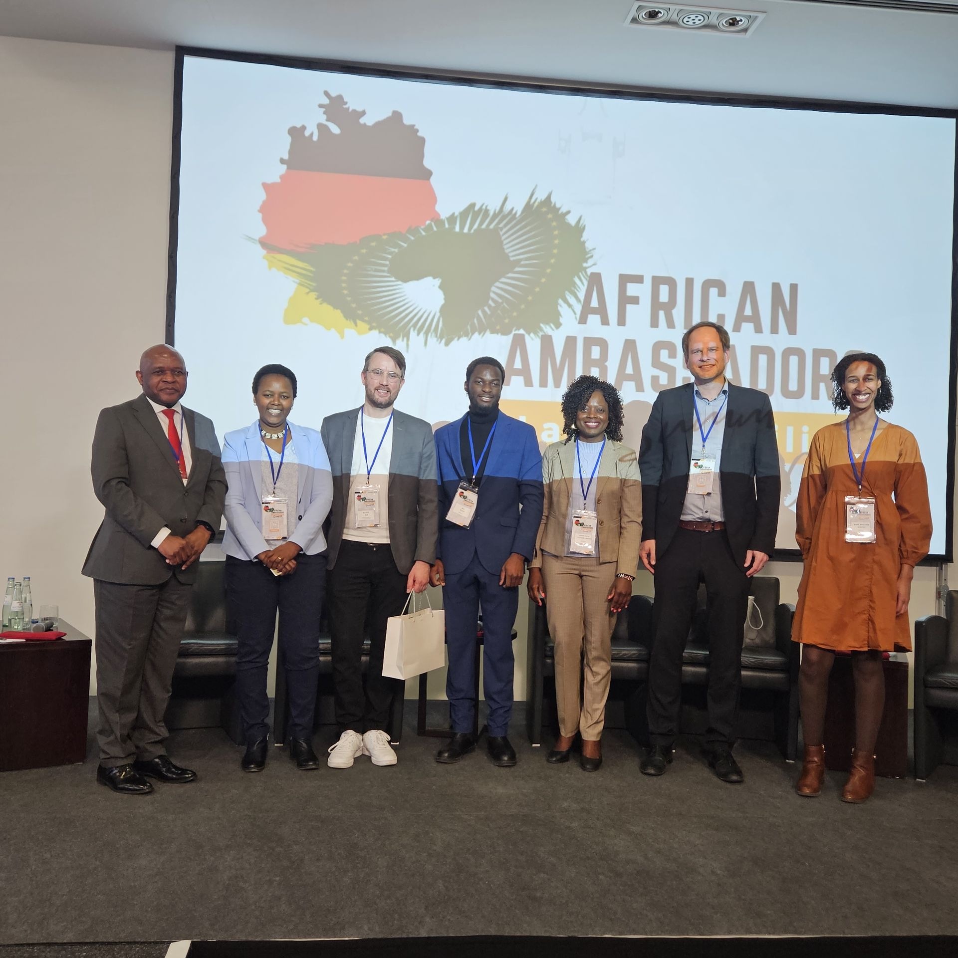 A group of people standing in front of a screen that says african ambassador