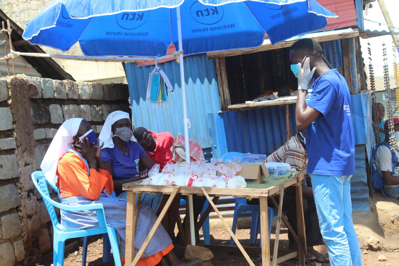 A man wearing a mask is talking on a cell phone in front of a blue umbrella.