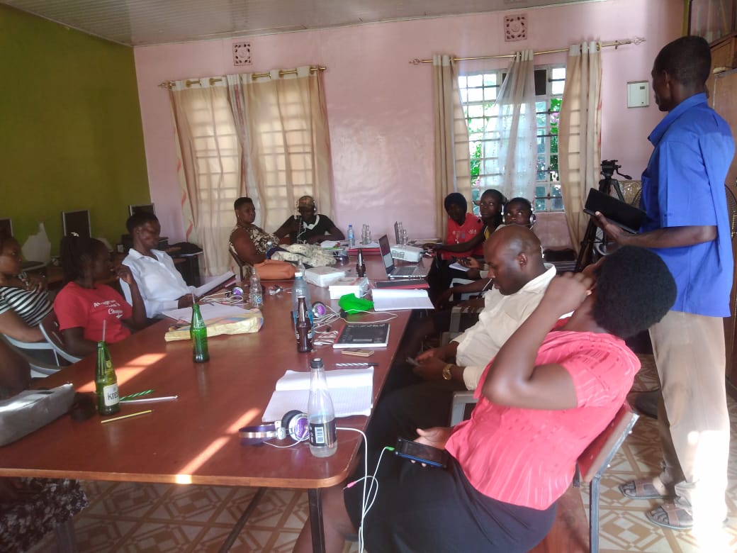 A man in a blue shirt is giving a presentation to a group of people sitting around a table