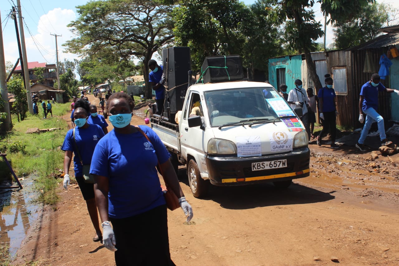 A group of people wearing masks are walking down a dirt road next to a truck.