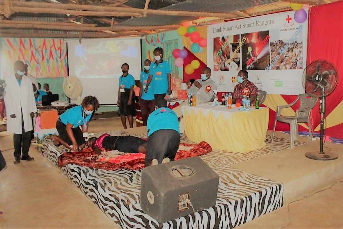 A group of people are standing around a person laying on a bed.