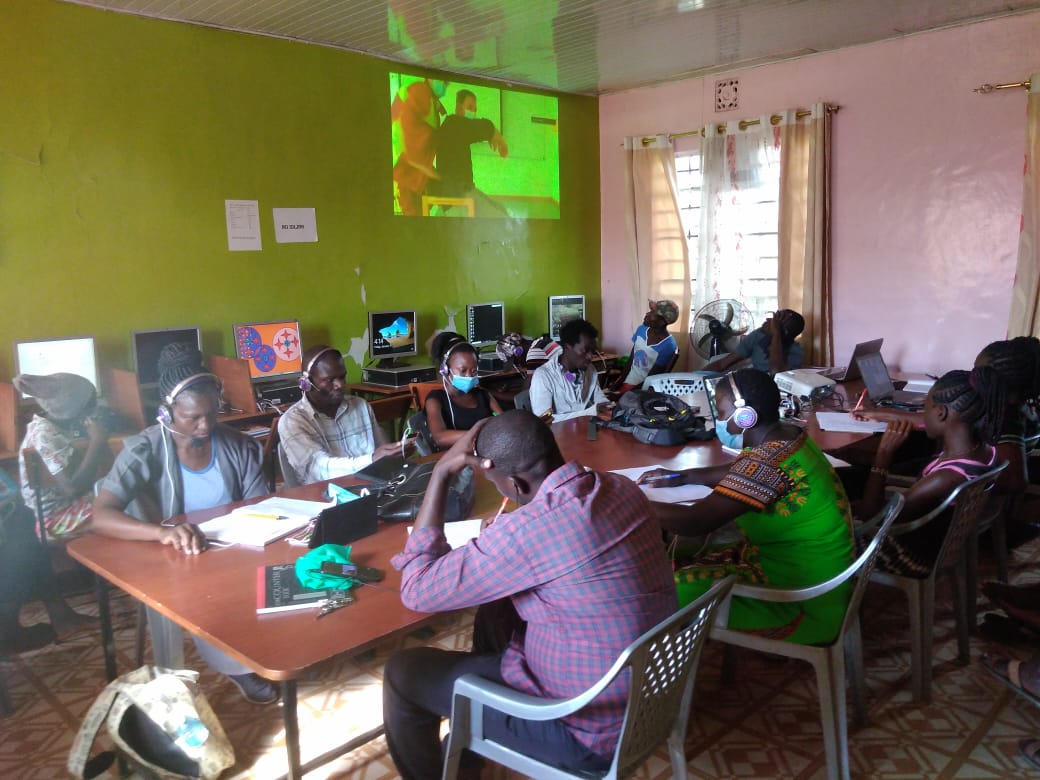 A group of people are sitting around a table in front of a projector screen.