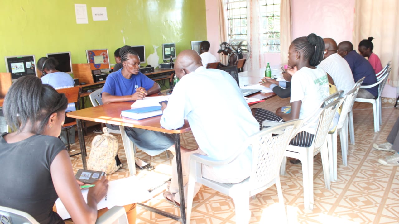 A group of people are sitting around a table in a room with computers
