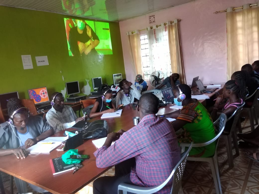 A group of people are sitting around a table in front of a projector screen.