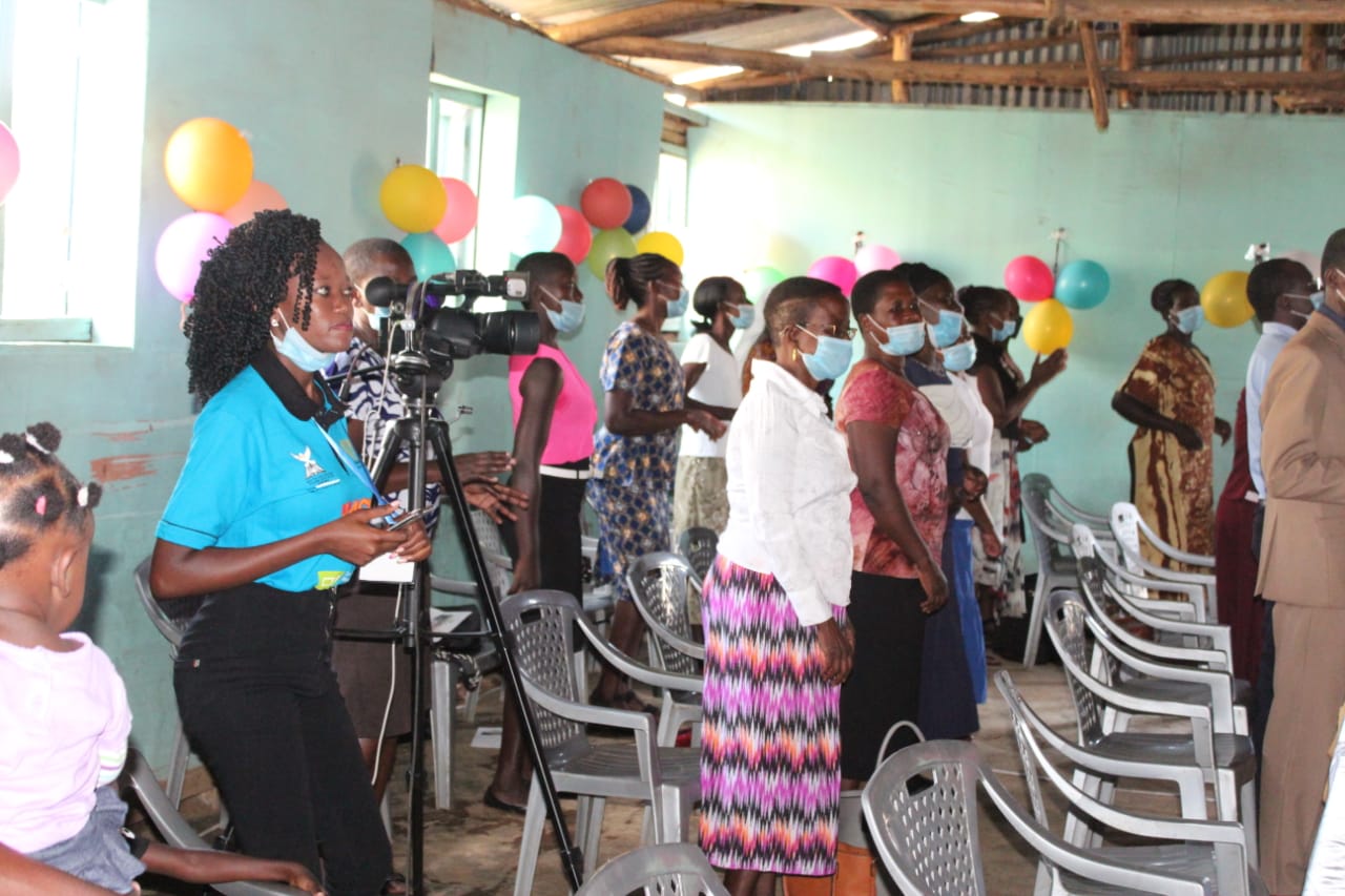 A group of people wearing face masks are standing in a room with chairs and balloons.