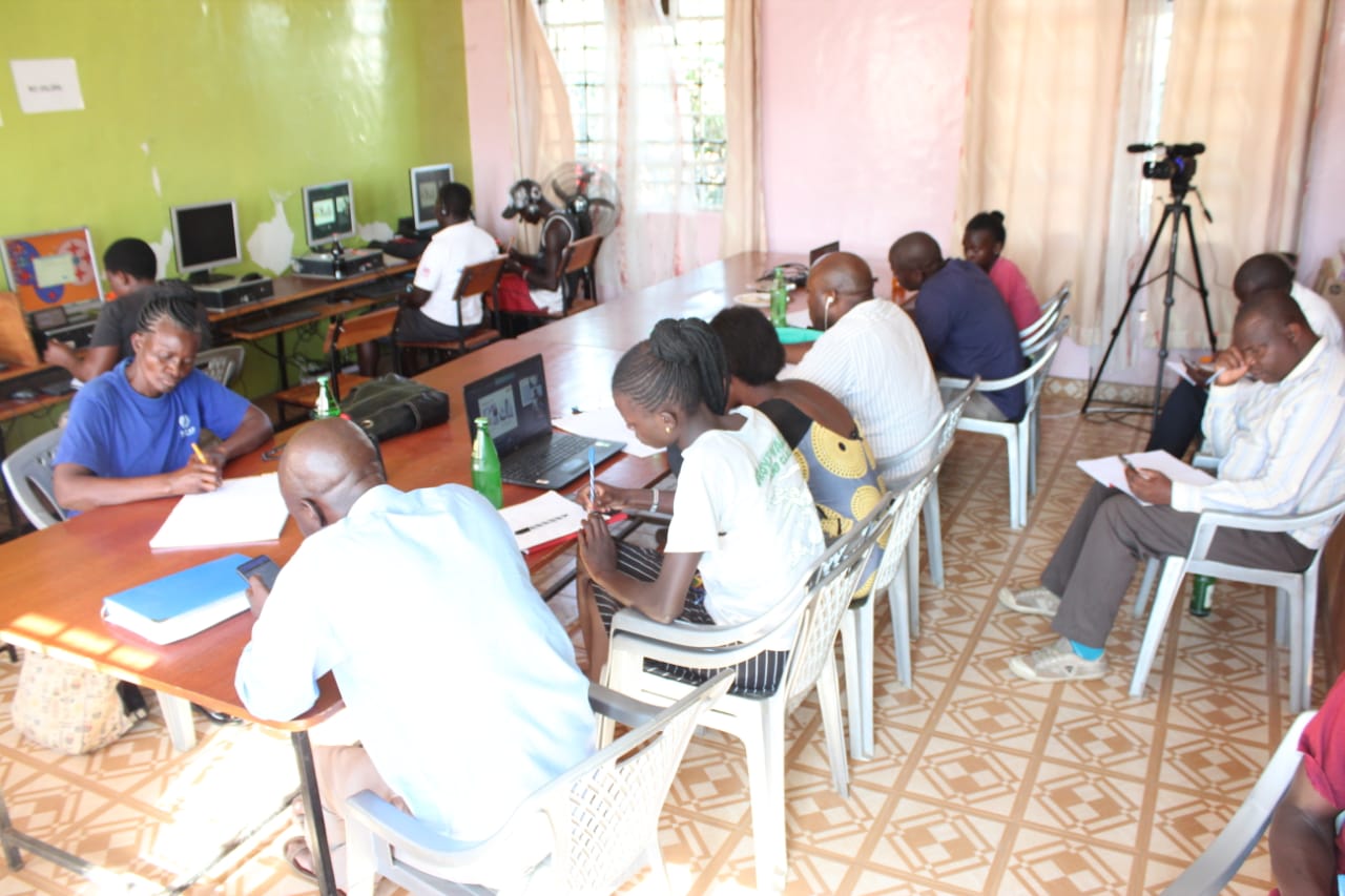 A group of people are sitting around a table with laptops