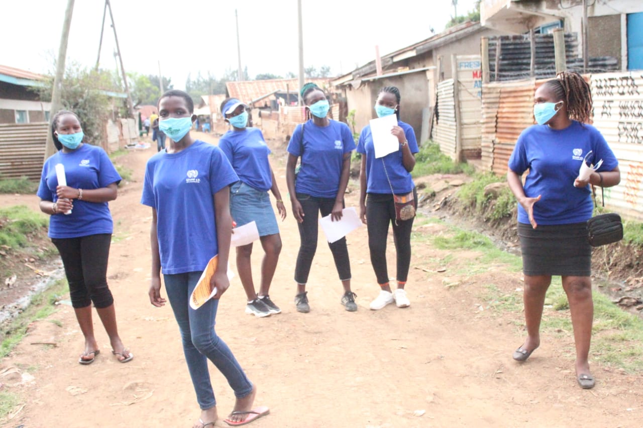 A group of women wearing face masks are standing on a dirt road.